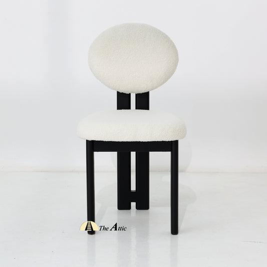 A wooden dining chair with padded seat and backrest, made from black-stained oak wood and upholstered in boucle fabric.