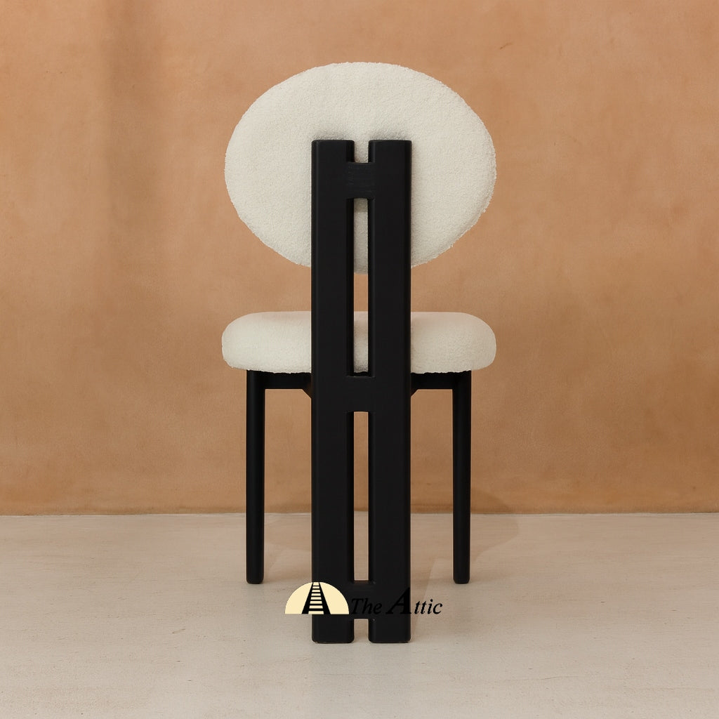 A wooden dining chair with padded seat and backrest, made from black-stained oak wood and upholstered in boucle fabric. The Attic Dubai