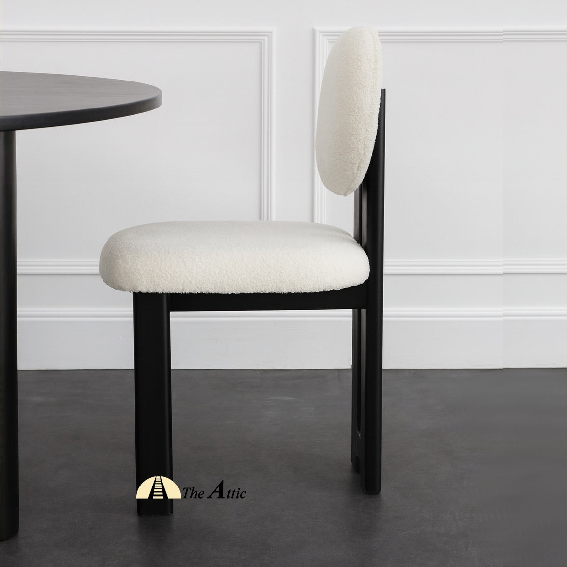 A wooden dining chair with padded seat and backrest, made from black-stained oak wood and upholstered in boucle fabric. The Attic Dubai