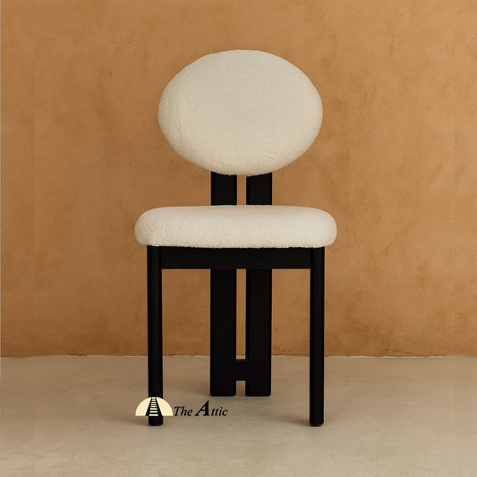 A wooden dining chair with padded seat and backrest, made from black-stained oak wood and upholstered in boucle fabric. The Attic Dubai
