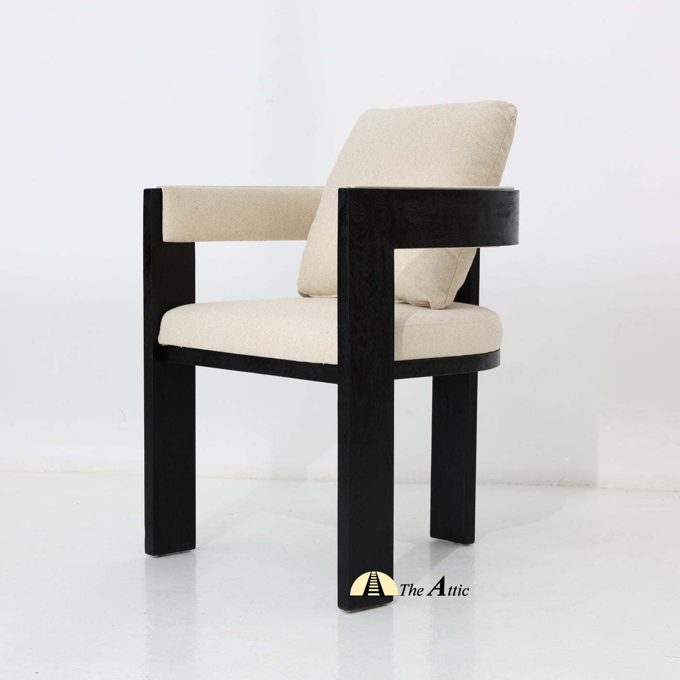 Chair with black wooden frame, padded seat, beige cushion, branded 'The Attic'