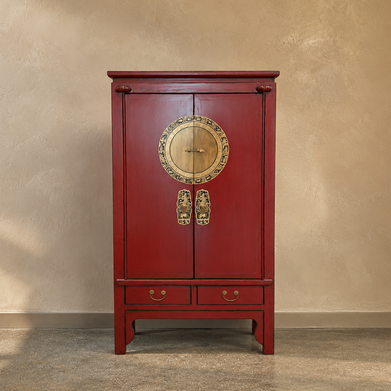 A traditional Chinese red wooden cabinet with brass hardware, featuring two doors with a round decorative brass emblem and brass handles, and two drawers at the bottom